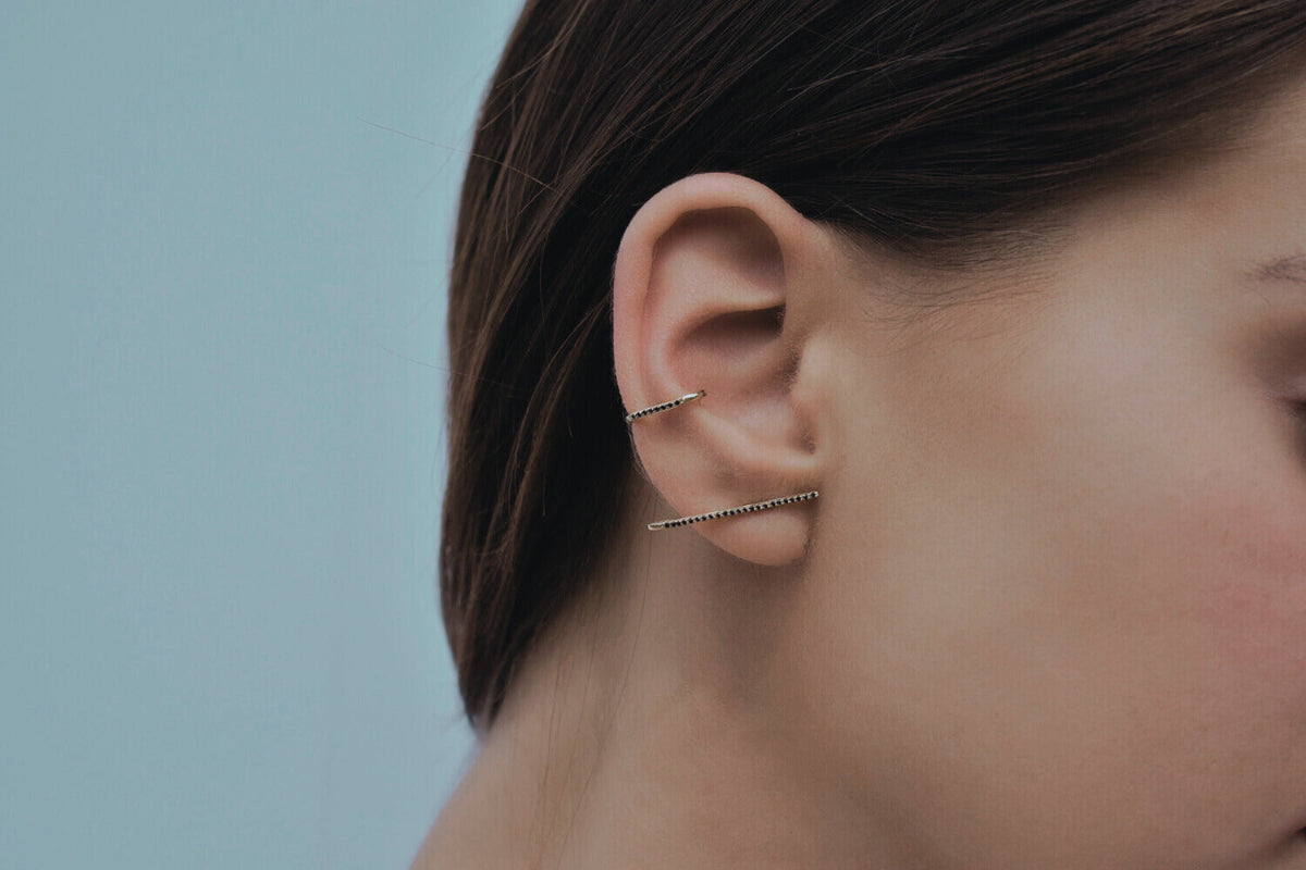 Close-up of a person wearing gold cuff earrings against a neutral background