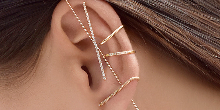 Close-up of an ear wearing gold earrings with a neutral background